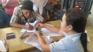 Emergency Shelter Assistance (ESA) Beneficiary signs ESA distribution sheet while MSWDO staff readies the cash to be given out to the beneficiary.